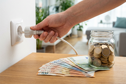 Hand zieht Stromstecker halb aus Steckdose, davor Euro-Scheine und Münzen als Symbol für Stromkostenersparnis
